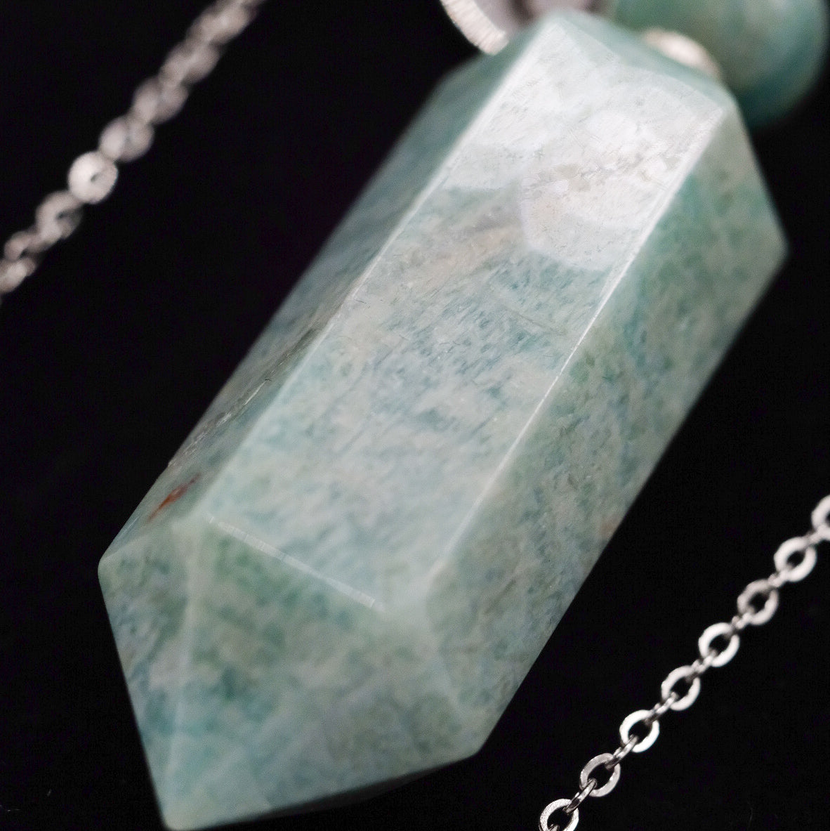Gros plan sur le pendentif en amazonite doTERRA monté sur une chaîne argentée, avec la pierre facettée mise en évidence sur fond noir.