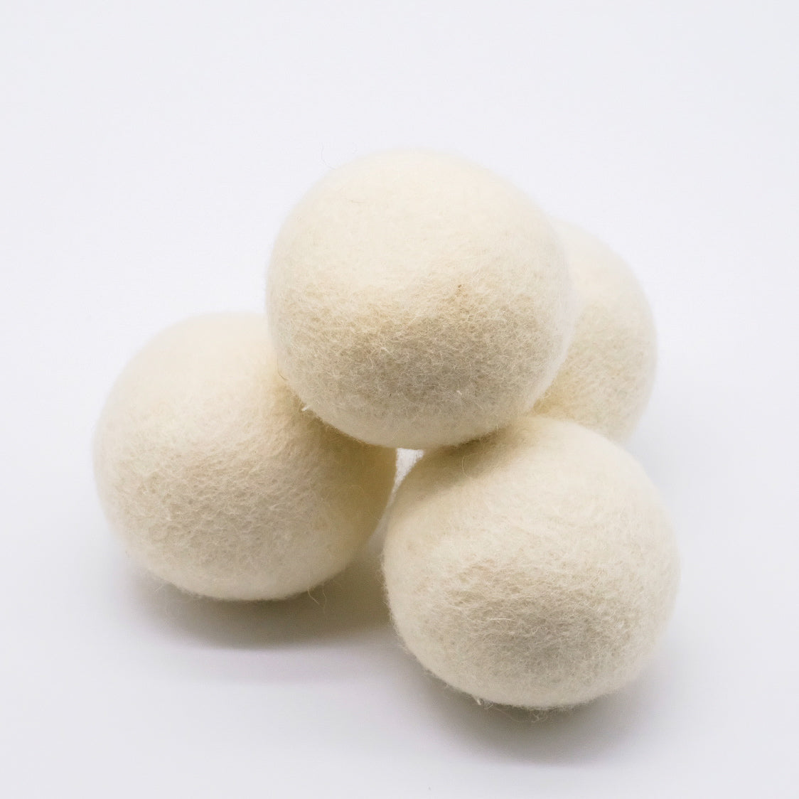 Ensemble de 4 balles de sécheuse en laine blanche, regroupées sur fond blanc.