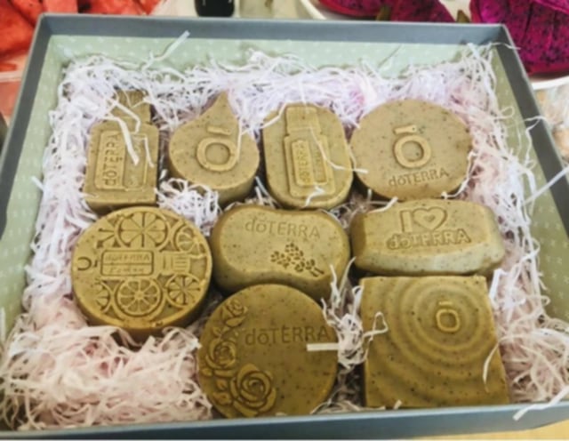 Assortiment de savons artisanaux doTERRA réalisés avec les moules en silicone violets, présentés dans un coffret garni de papier blanc.