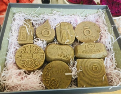 Assortiment de savons artisanaux doTERRA réalisés avec les moules en silicone violets, présentés dans un coffret garni de papier blanc.