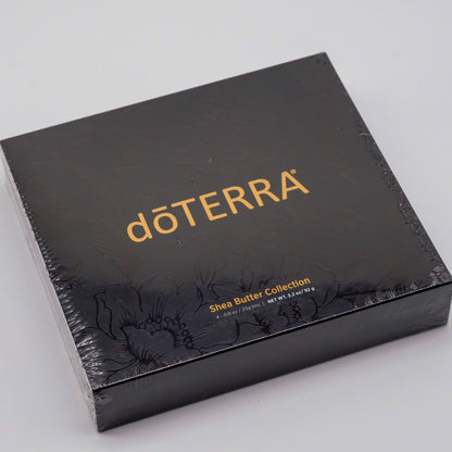 Coffret noir doTERRA Collection beurre de karité sous emballage plastique, avec logo doré et motif floral ton sur ton.