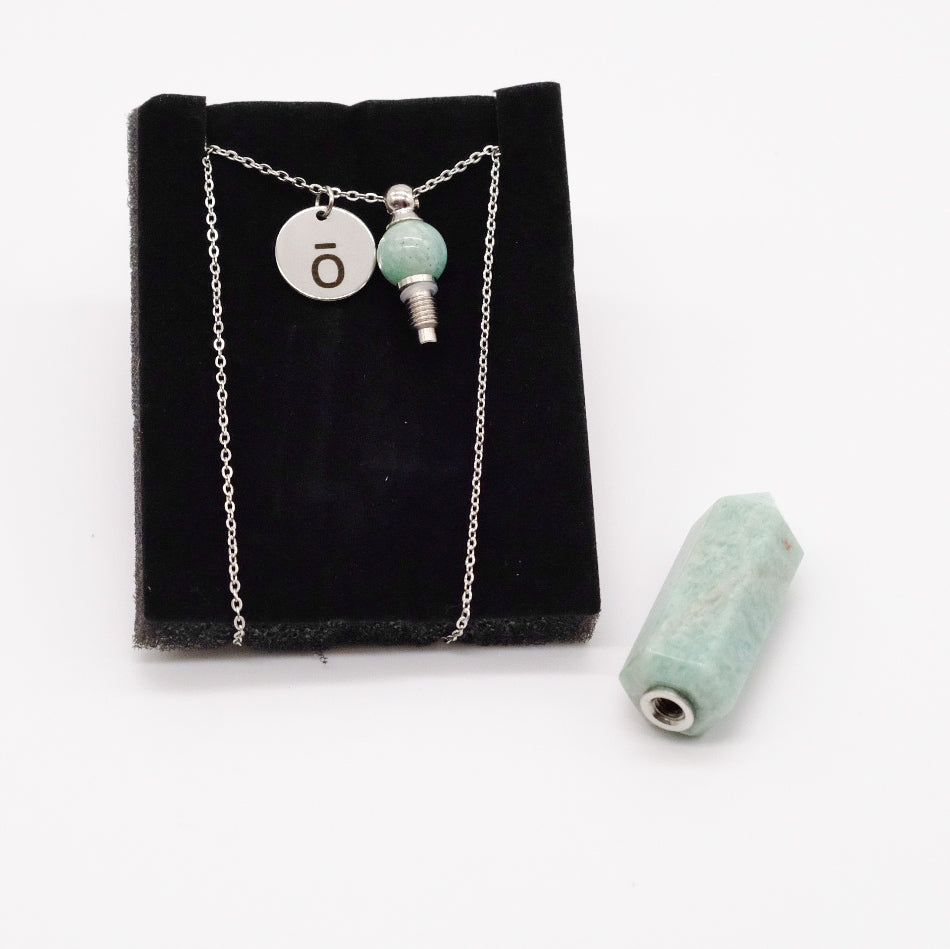 Collier pendentif en amazonite doTERRA avec flacon, présenté sur un support noir avec la pierre amovible retirée et posée à côté.