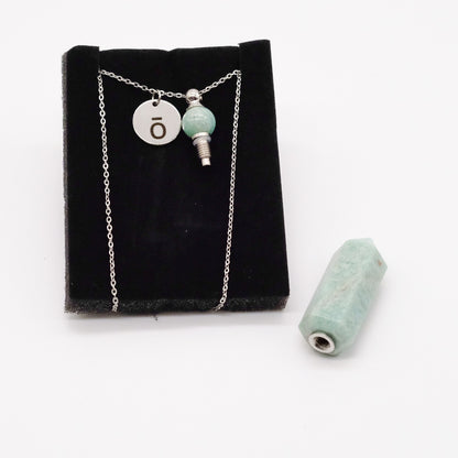 Collier pendentif en amazonite doTERRA avec flacon, présenté sur un support noir avec la pierre amovible retirée et posée à côté.