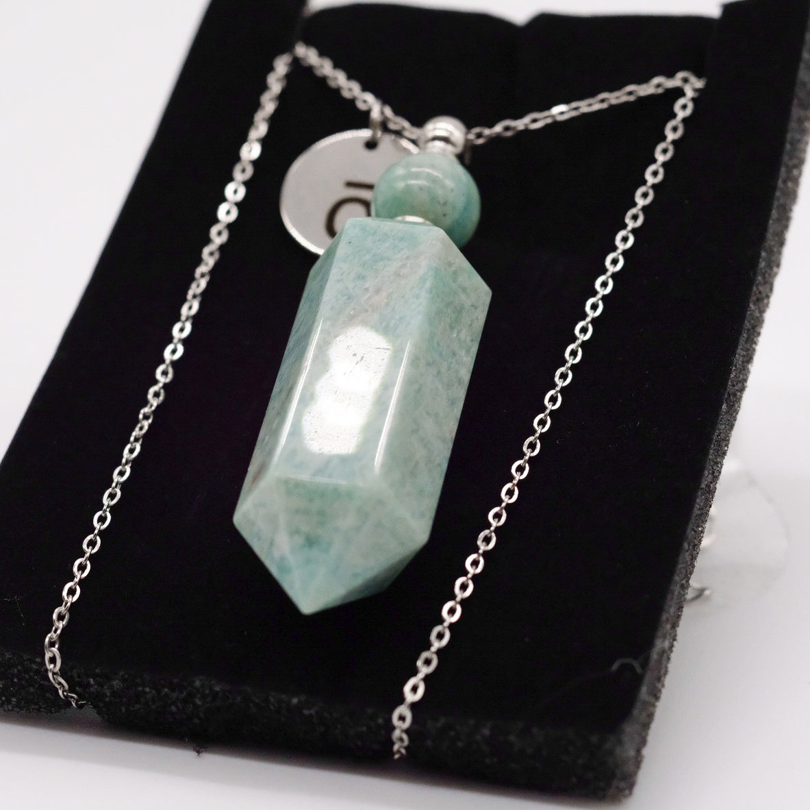 Collier pendentif en amazonite doTERRA avec flacon, présenté sur un support noir.
