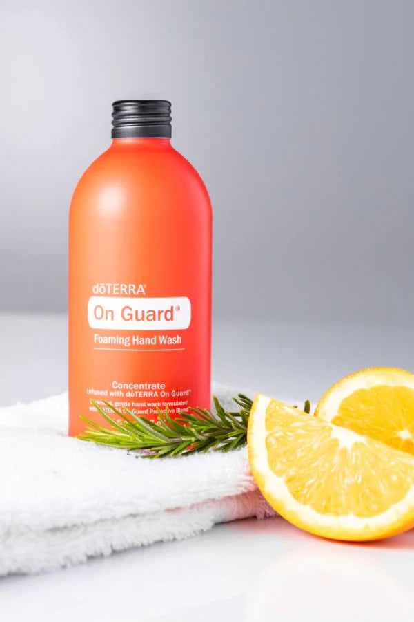 Concentré pour savon moussant à mains On Guard doTERRA, bouteille orange avec demi-orange, branche de romarin et serviette blanche.