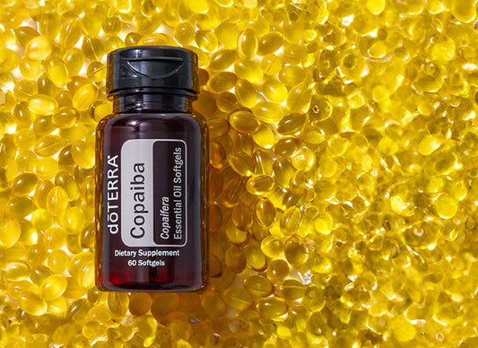 Bouteille de Copaiba softgels doTERRA, format 60 gélules, posée sur un fond de capsules jaunes translucides.