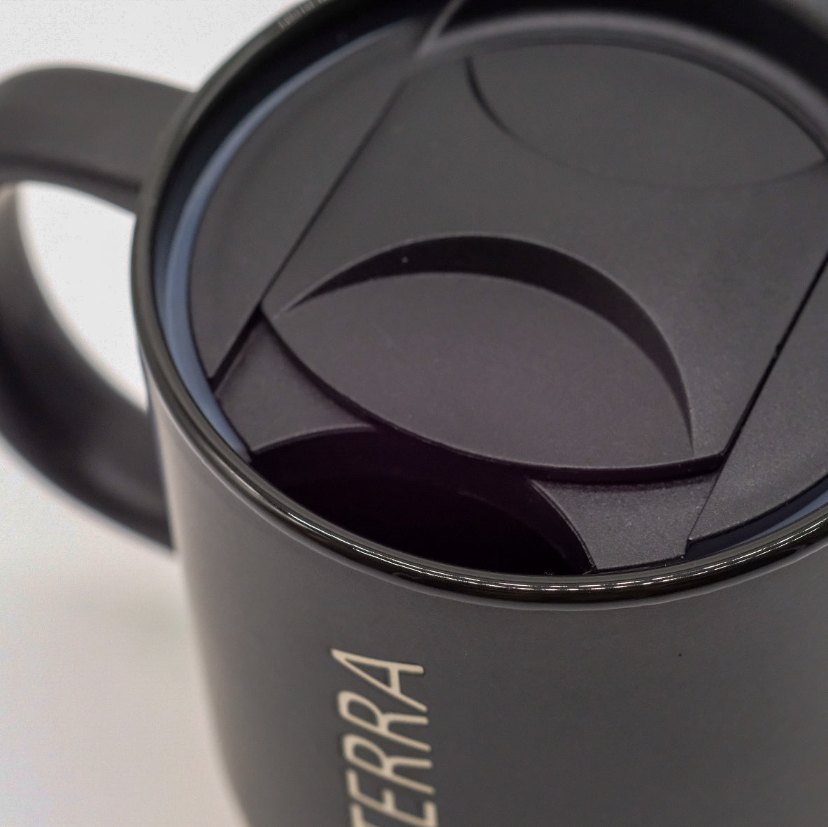 Gros plan sur le couvercle noir et la poignée d’une tasse doTERRA noire.