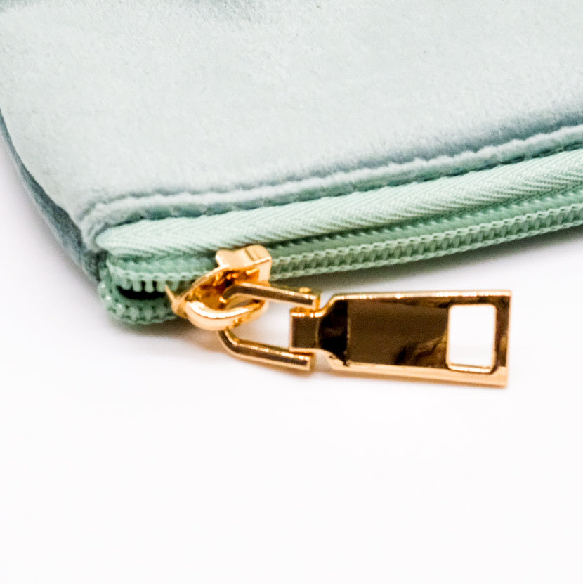 Gros plan sur la fermeture éclair dorée d’une pochette en velours vert sauge.