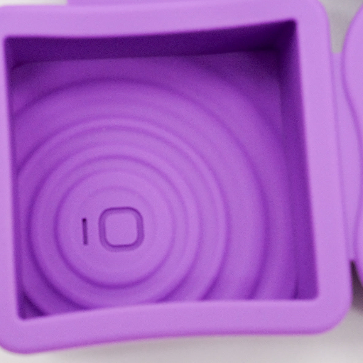 Gros plan sur un moule carré en silicone violet doTERRA avec motif embossé de cercles concentriques au fond.