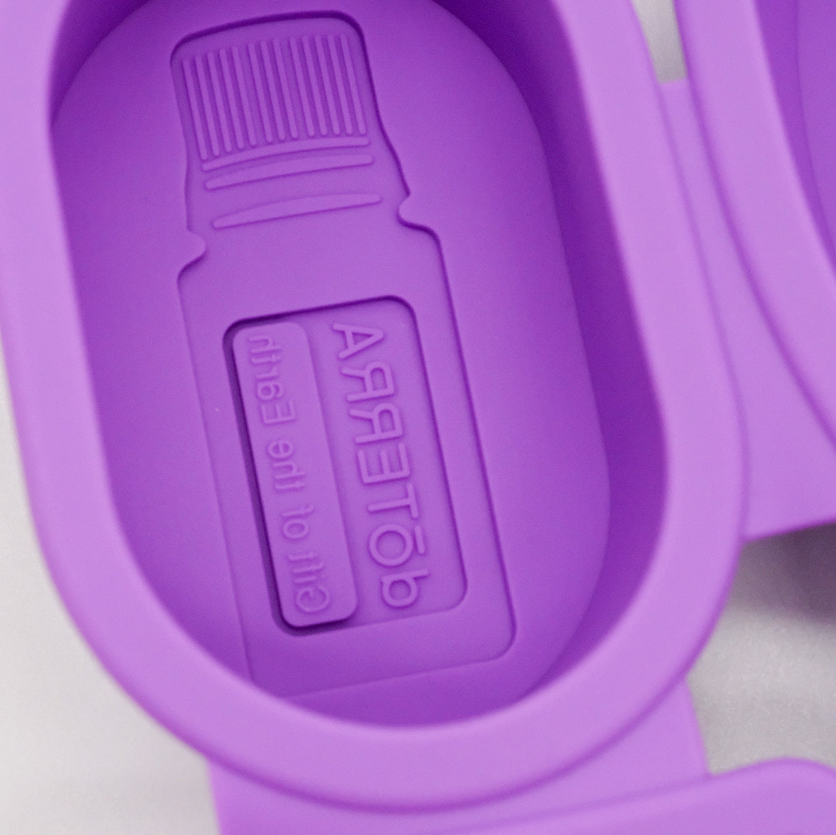 Gros plan sur un moule ovale en silicone violet doTERRA avec motif embossé de bouteille d’huile essentielle au fond.