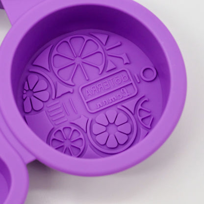 Gros plan sur un moule rond en silicone violet doTERRA avec motif embossé d’agrumes et logo au fond.