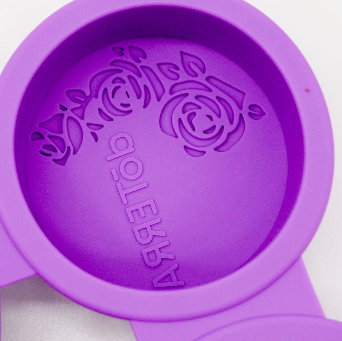 Gros plan sur un moule rond en silicone violet doTERRA avec motif floral embossé et logo inversé au fond.