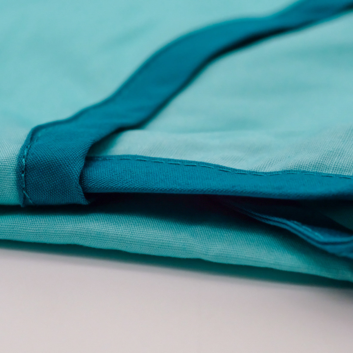 Gros plan sur la Robe Réutilisable AromaTouch pliée, montrant le tissu bleu pâle et la bordure turquoise.