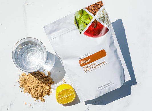Sachet doTERRA Fiber avec huile essentielle de citron, poudre de fibres, demi-citron et verre d’eau sur fond blanc.