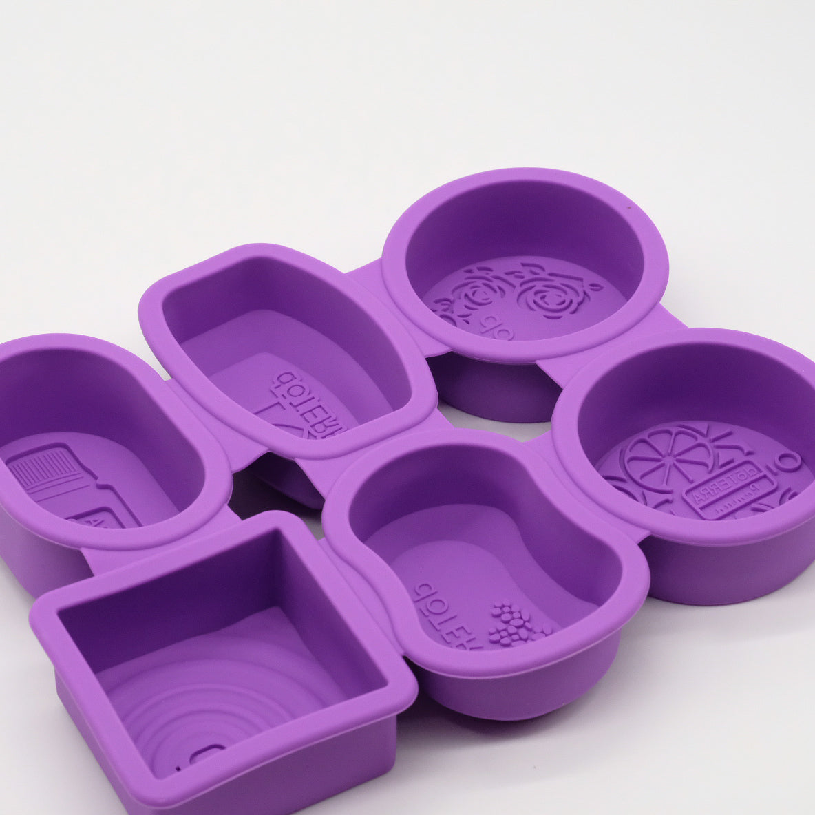 Ensemble de moules en silicone violets doTERRA avec formes variées, incluant des moules ronds, carrés et rectangulaires avec motifs embossés.