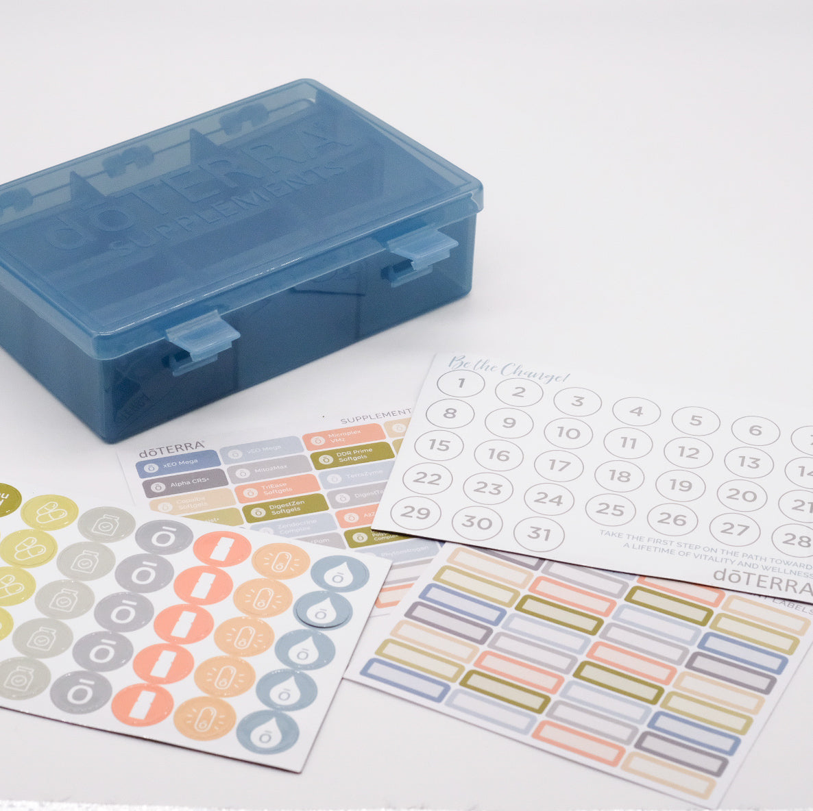 Grand pilulier bleu translucide doTERRA pour suppléments, présenté avec feuilles d’autocollants colorés et calendrier numéroté.