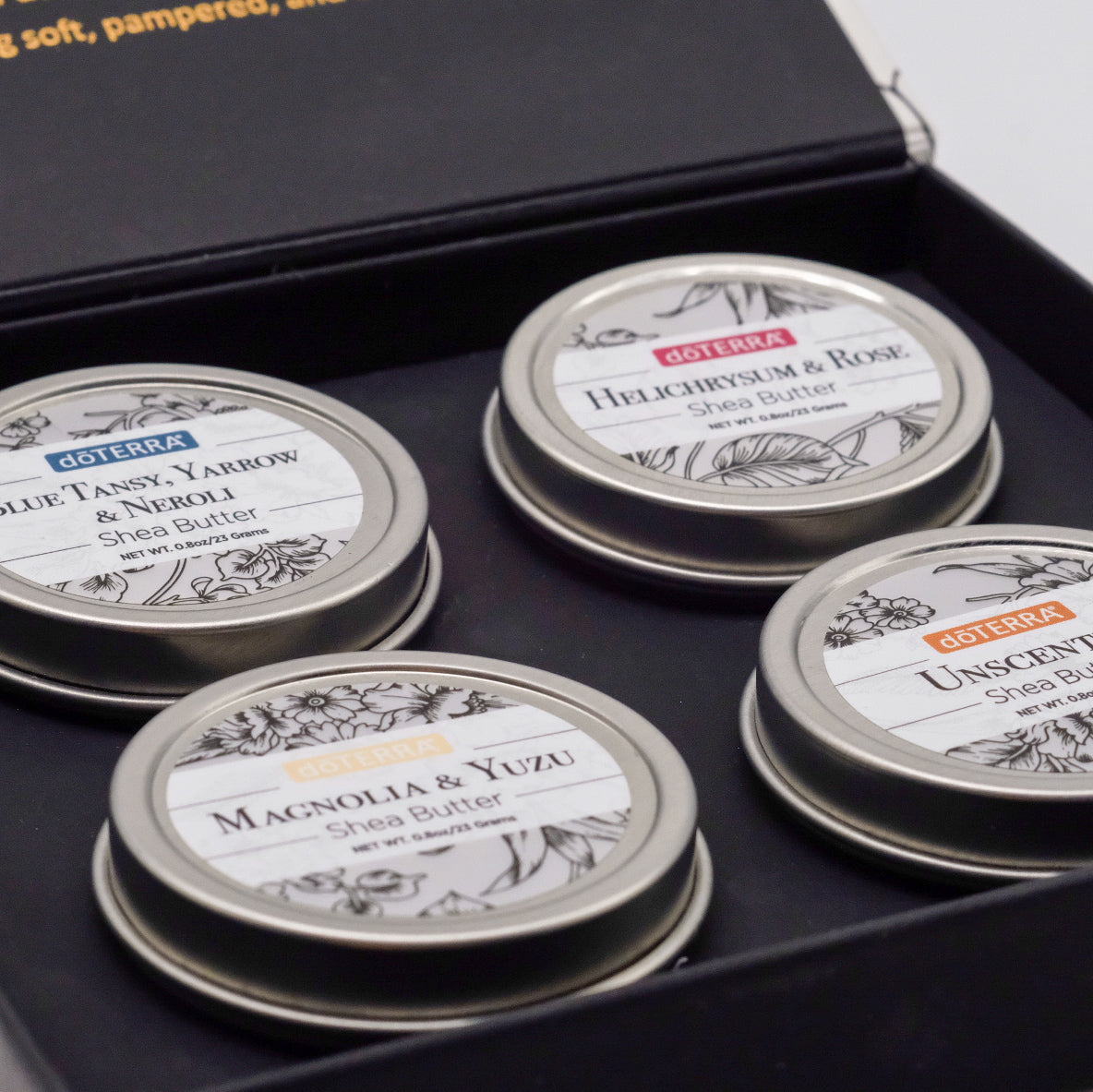 Gros plan sur quatre baumes de la collection beurre de karité doTERRA dans leur coffret : Blue Tansy, Yarrow & Neroli, Helichrysum & Rose, Magnolia & Yuzu, et une version sans parfum.