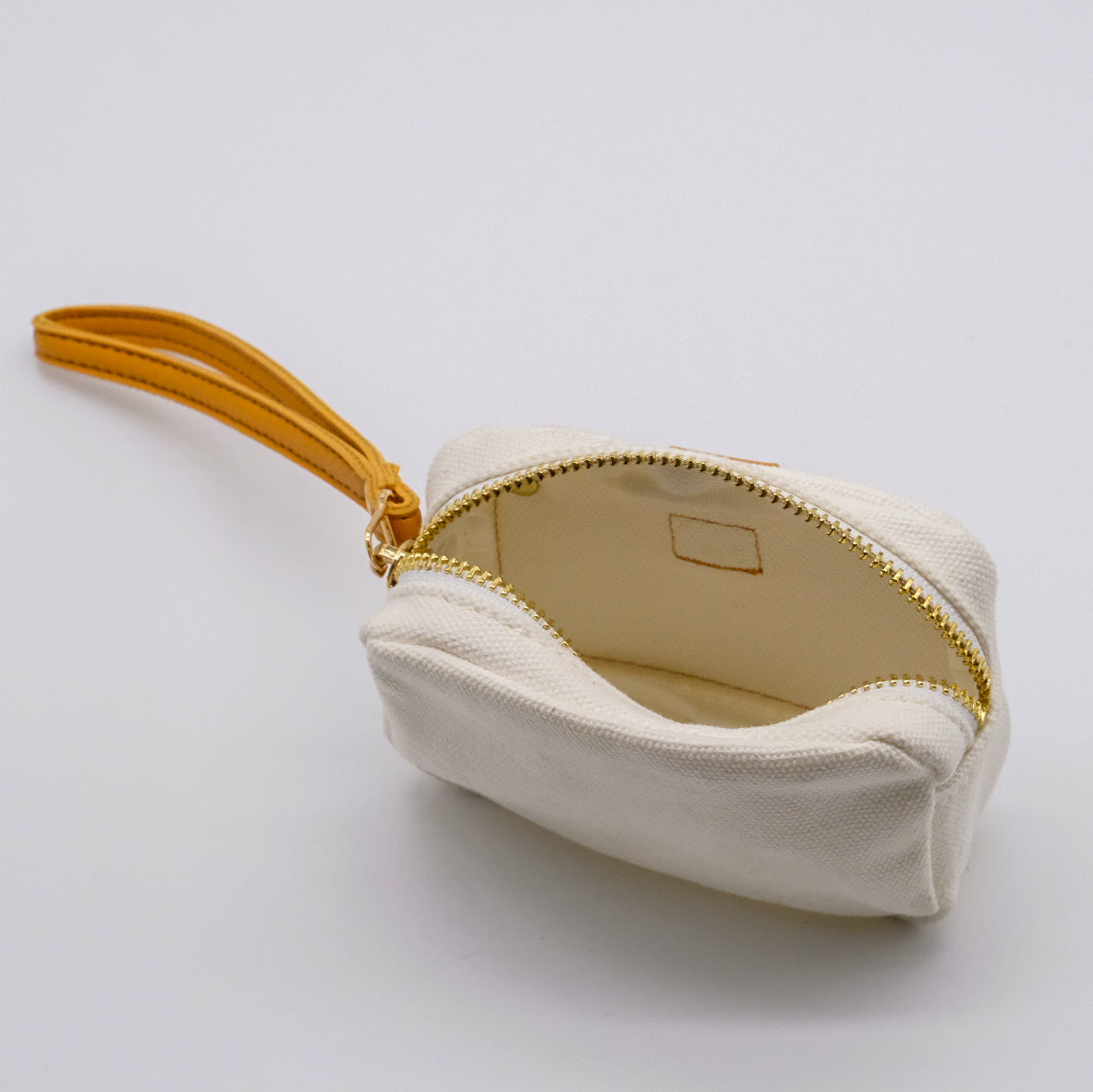 Mini étui blanc doTERRA ouvert, avec intérieur clair, fermeture éclair dorée et attache-poignet camel.