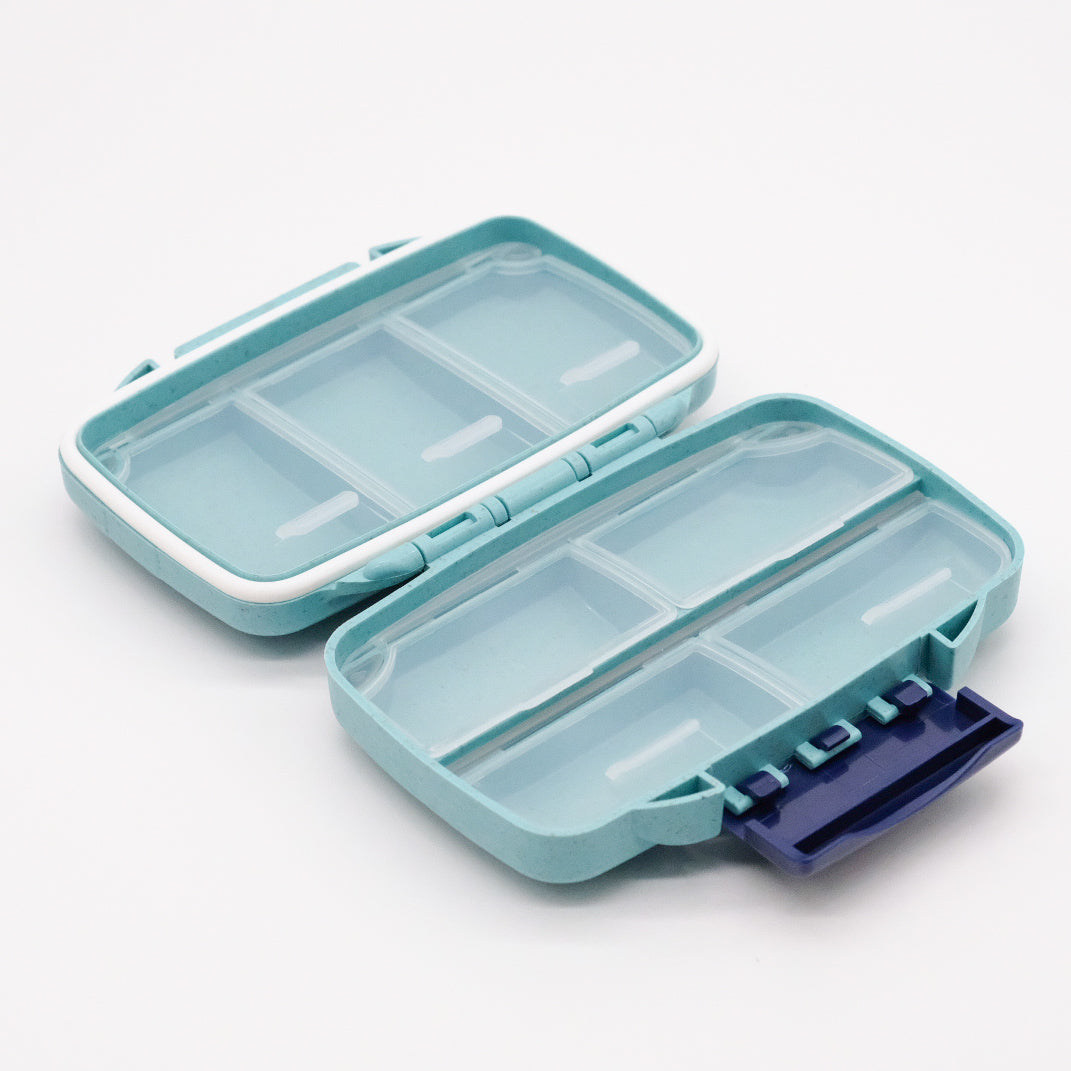 Pilulier portatif turquoise doTERRA ouvert, avec compartiments translucides vides et fermoir violet visible sur l’un des boîtiers.