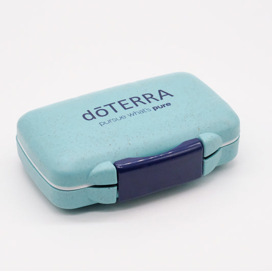 Petit pilulier portatif turquoise doTERRA, boîtier rectangulaire compact avec fermoir violet, présenté fermé sur fond clair.