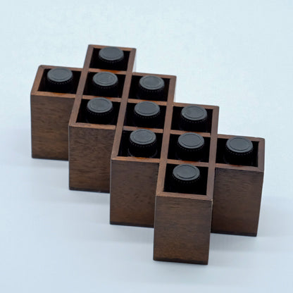 Présentoir en bois foncé, avec plusieurs compartiments rectangulaires contenant des bouteilles d’huiles essentielles, vu en angle.