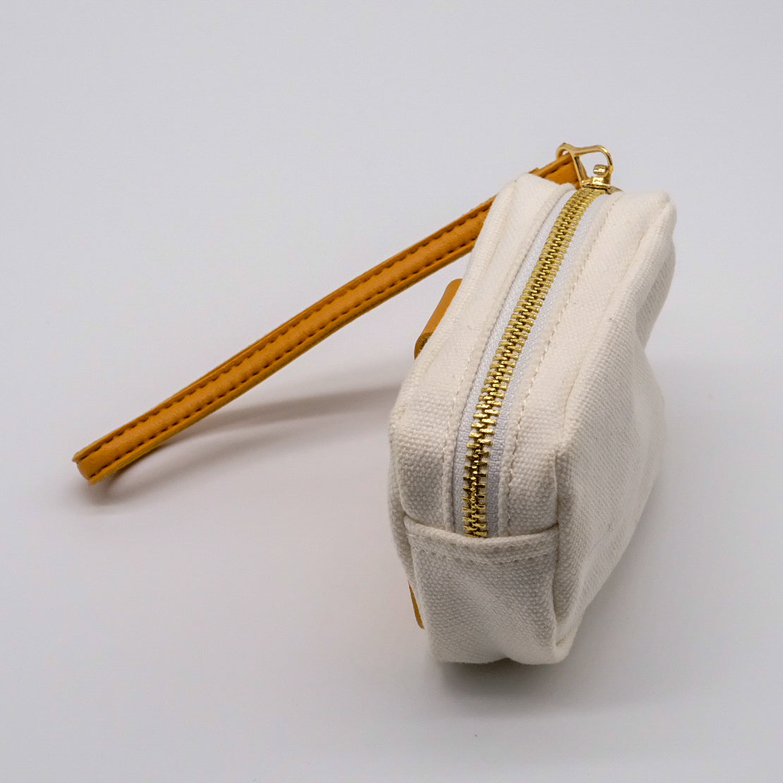 Vue de profil d’un mini étui blanc doTERRA avec fermeture éclair dorée et attache-poignet camel.