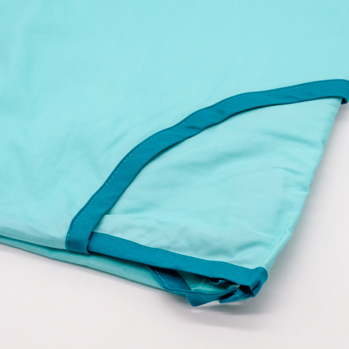 Robe Réutilisable AromaTouch pliée, en tissu bleu pâle avec bordure turquoise.